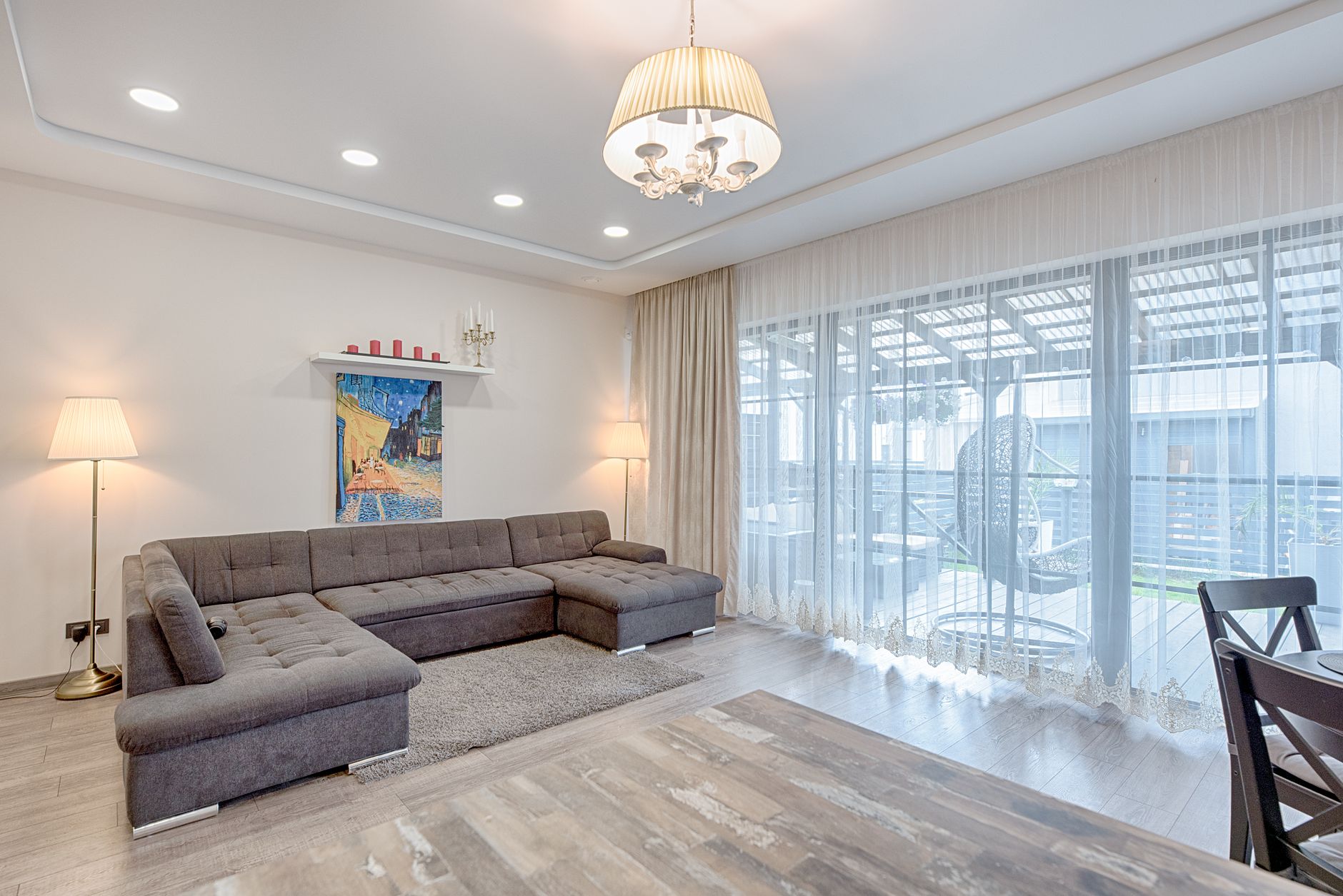 salon moderne avec un canapé d'angle gris, un lustre à abat-jour au plafond, des spots encastrés et un lampadaire dans un angle
