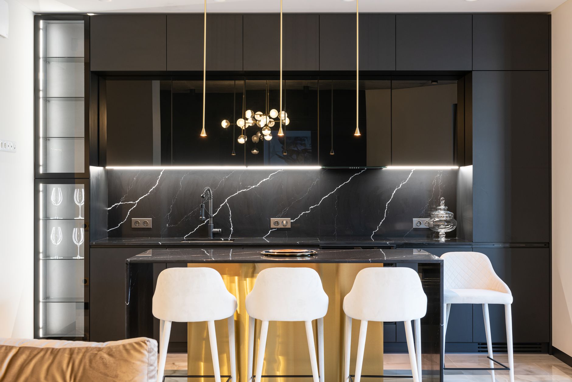 cuisine noire avec une ligne de LED continue sous les meubles hauts qui éclaire une crédence en marbre noir, suspensions fines au-dessus de l'îlot
