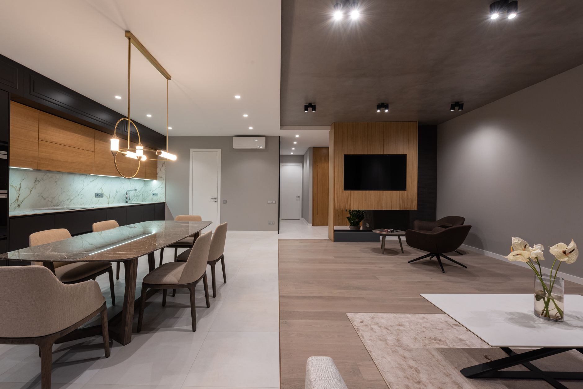 longue table à manger en pierre sous une suspension linéaire dorée, chaises tapissées, cuisine ouverte en arrière-plan